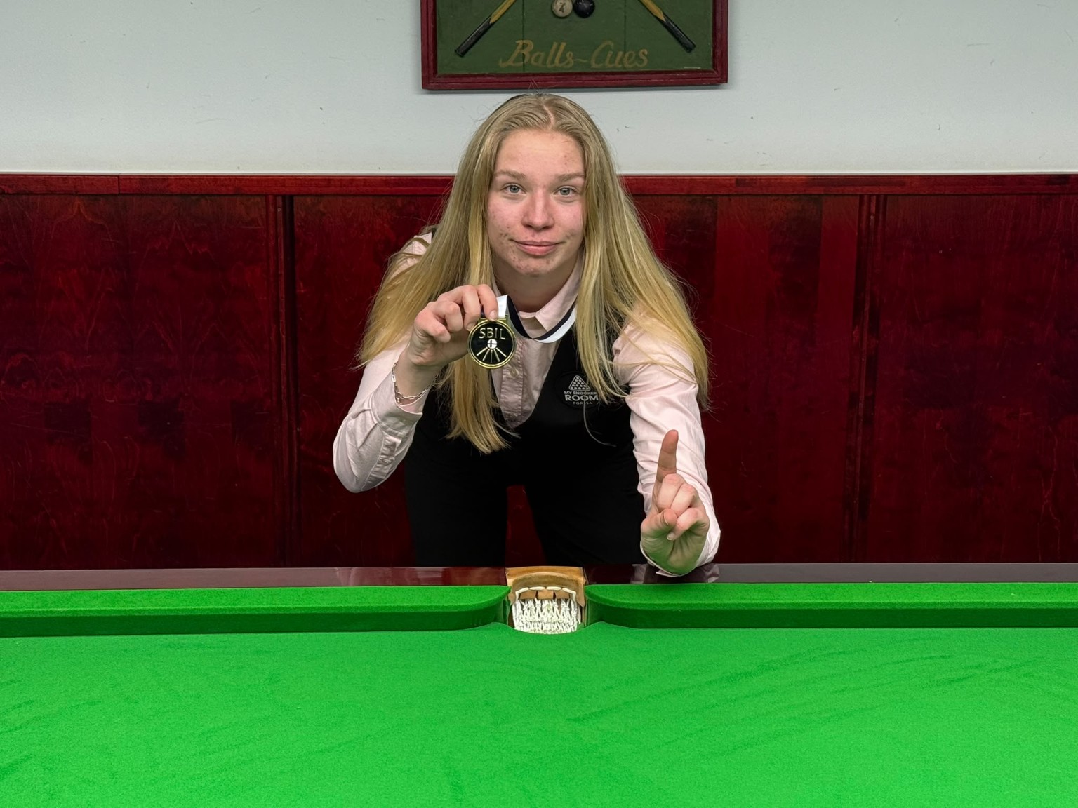 Annika Suominen esittelee kultamitaliaan snookerpöydän äärellä